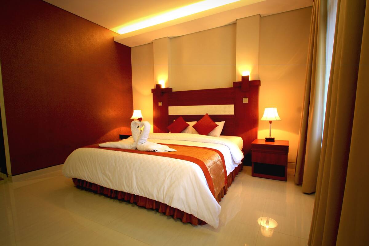 Une chambre d’hôtel avec un grand lit, deux tables de chevet avec des lampes et un mur d’accent rouge.