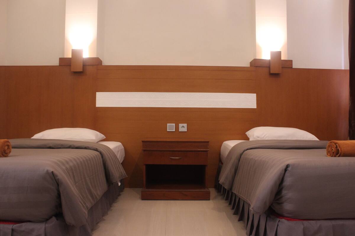 Une chambre d’hôtel avec deux lits, une tête de lit en bois, des lampes de chevet et une petite table de chevet en bois.