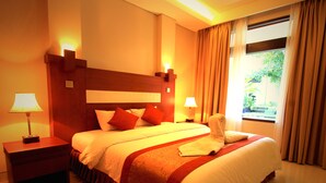 A hotel room with a large bed, two bedside tables with lamps, a wooden headboard, and a window with curtains. - Jesens Inn 2 (Kuta)