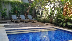 A swimming pool with tiled steps, surrounded by lounge chairs and lush greenery. - Jesens Inn 2 (Kuta)