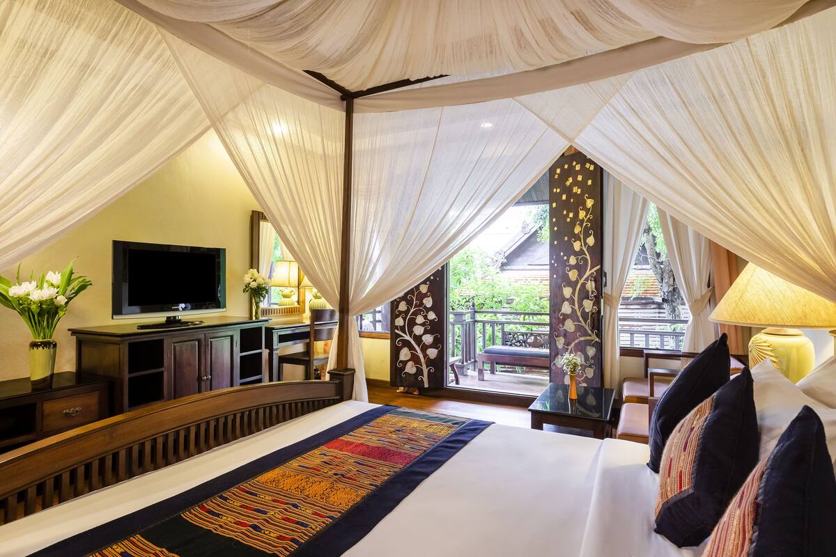 A bedroom with a large bed, a TV, and a view of a balcony.