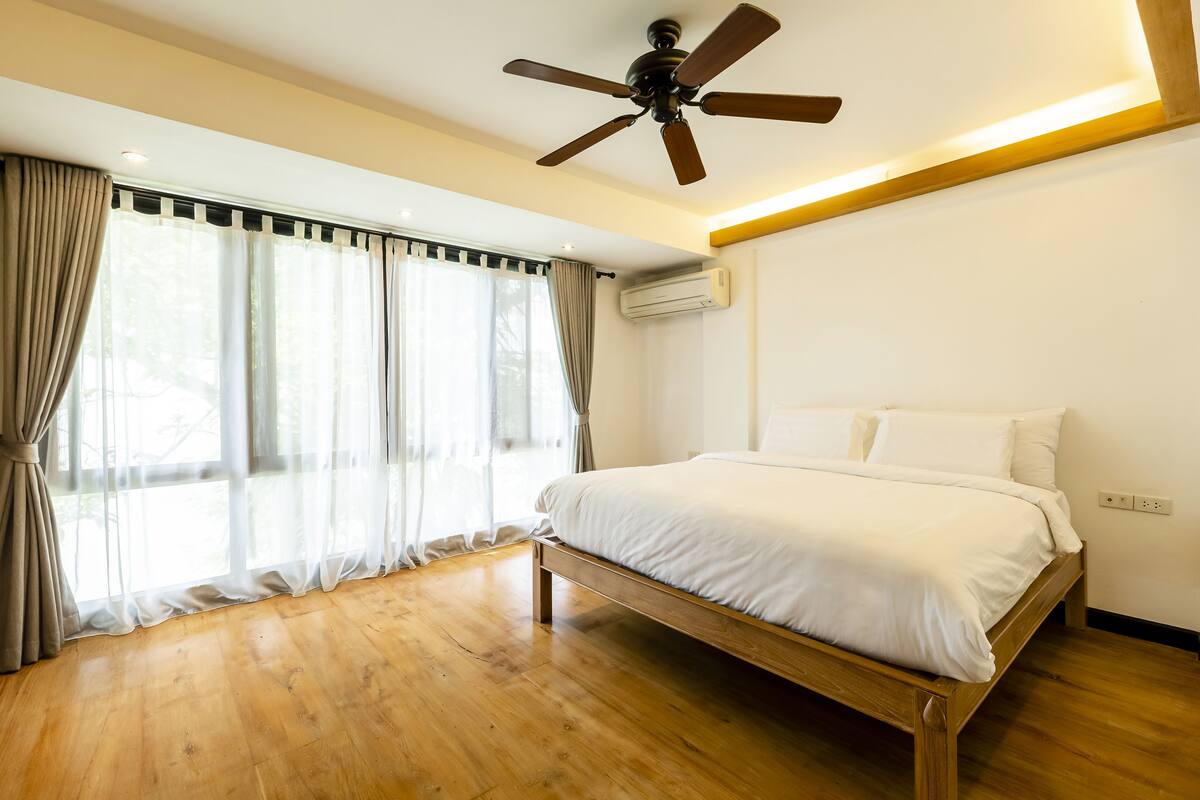 A bedroom with a wooden bed, a ceiling fan, and large windows with curtains.