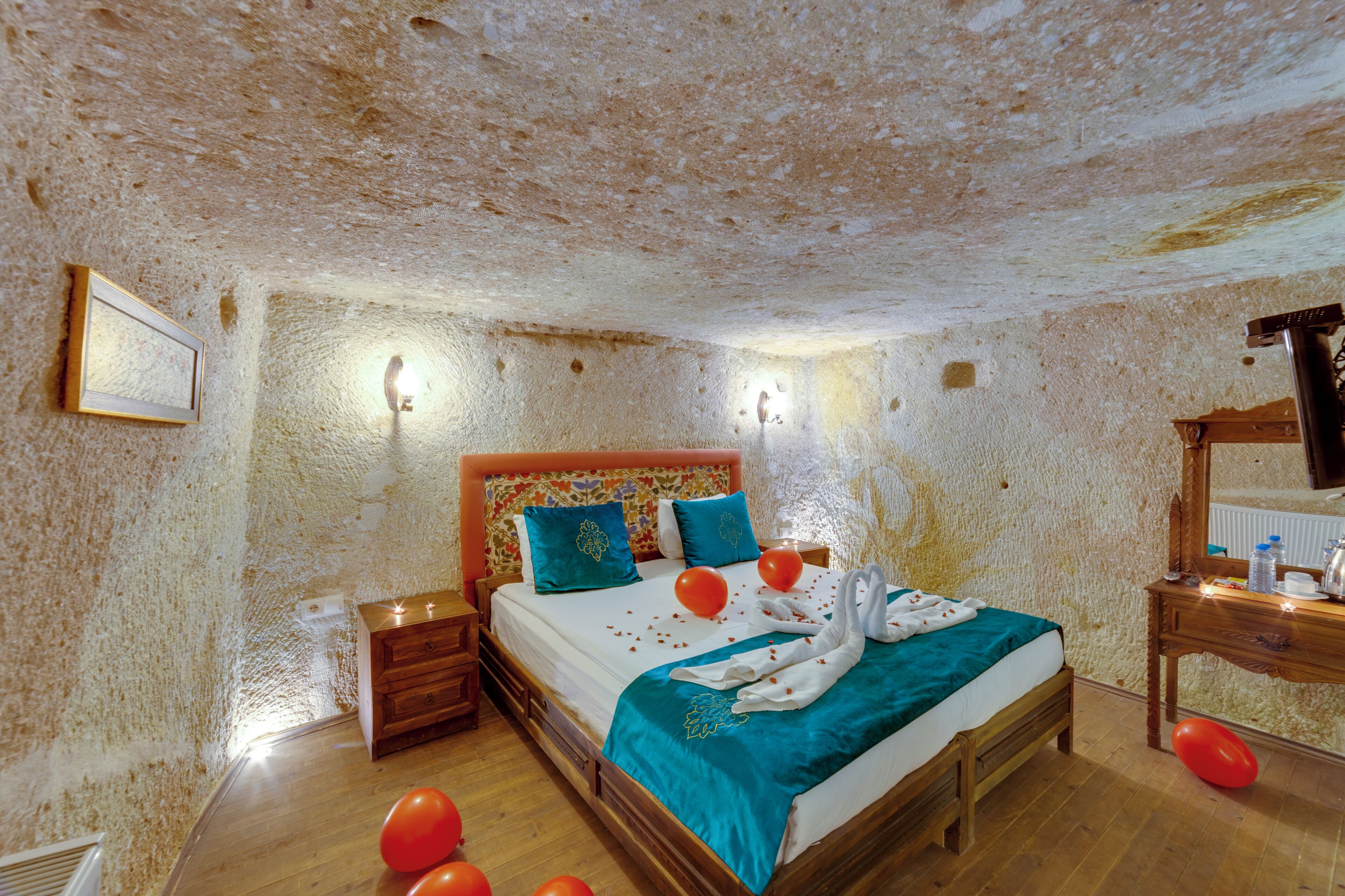 A bedroom with a rustic stone wall, a wooden bed with teal bedding, and a wooden nightstand.