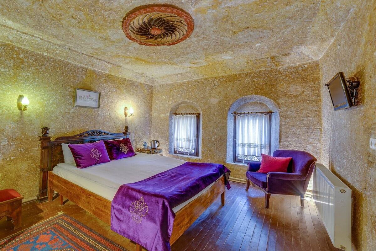 Ein Schlafzimmer mit einem hölzernen Bett, violetter Bettwäsche, einem kleinen Tisch und zwei Stühlen sowie einem Heizkörper.