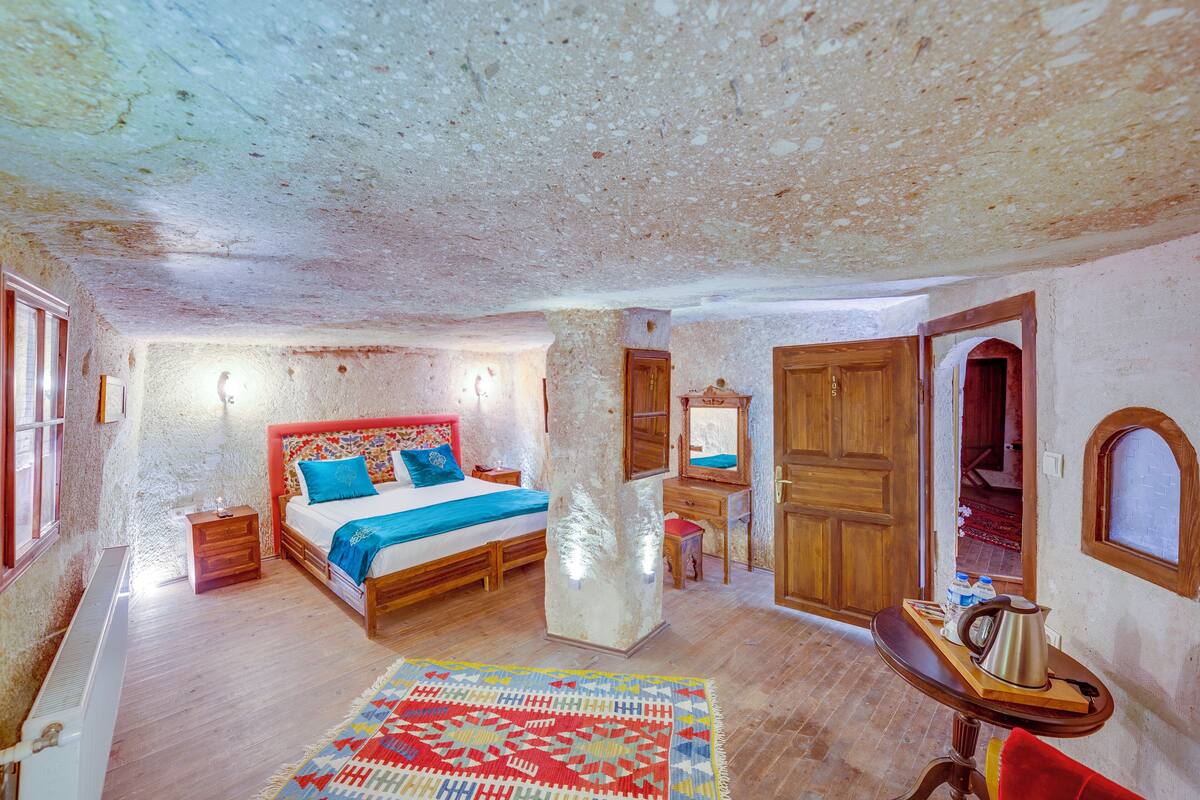 Ein Schlafzimmer mit einem hölzernen Bett, einem Nachttisch, einer Kommode, einem Spiegel und einem kleinen Tisch mit Wasserkocher.