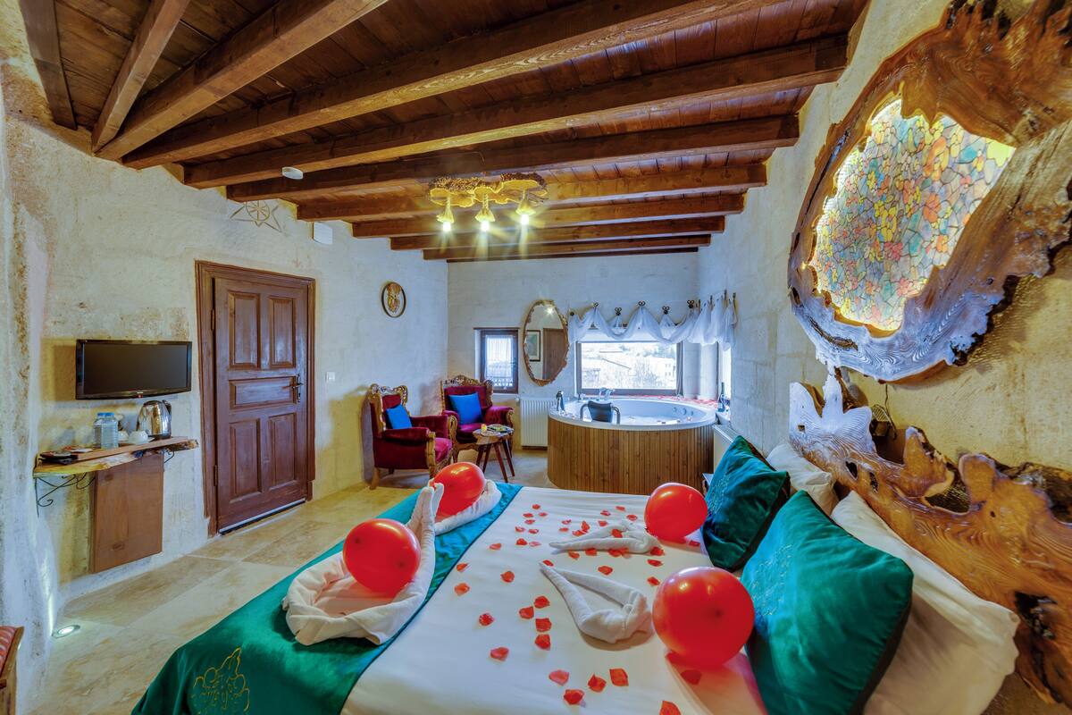 Ein Zimmer mit Holzboden, einem Bett mit roten Ballons, einem hölzernen Kopfteil, einer Holzkommode, einem Fernseher, einem Sessel, einem Fenster und einem Spiegel.