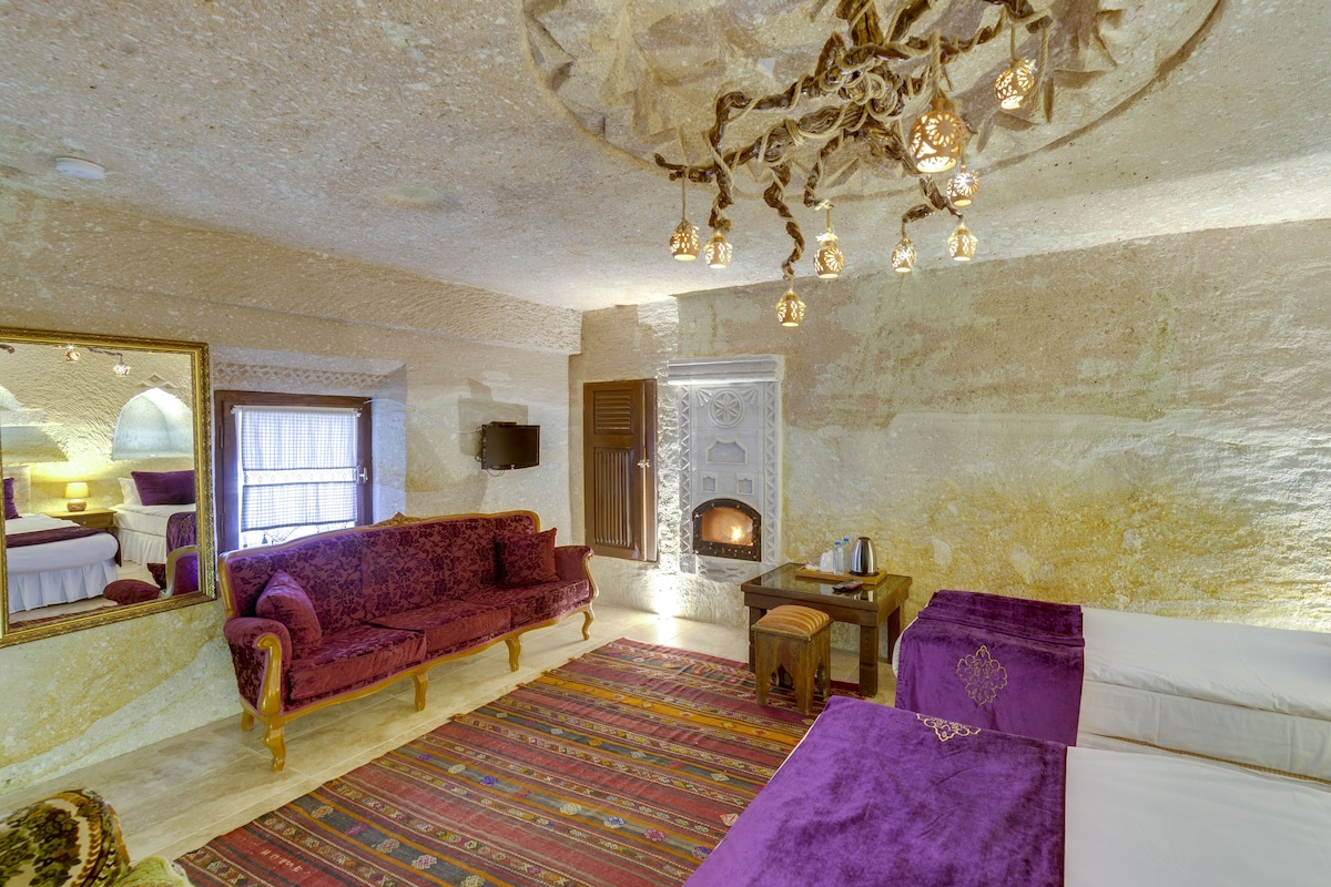 Una habitación con sofá rojo, sillón morado, alfombra estampada, chimenea y candelabro.