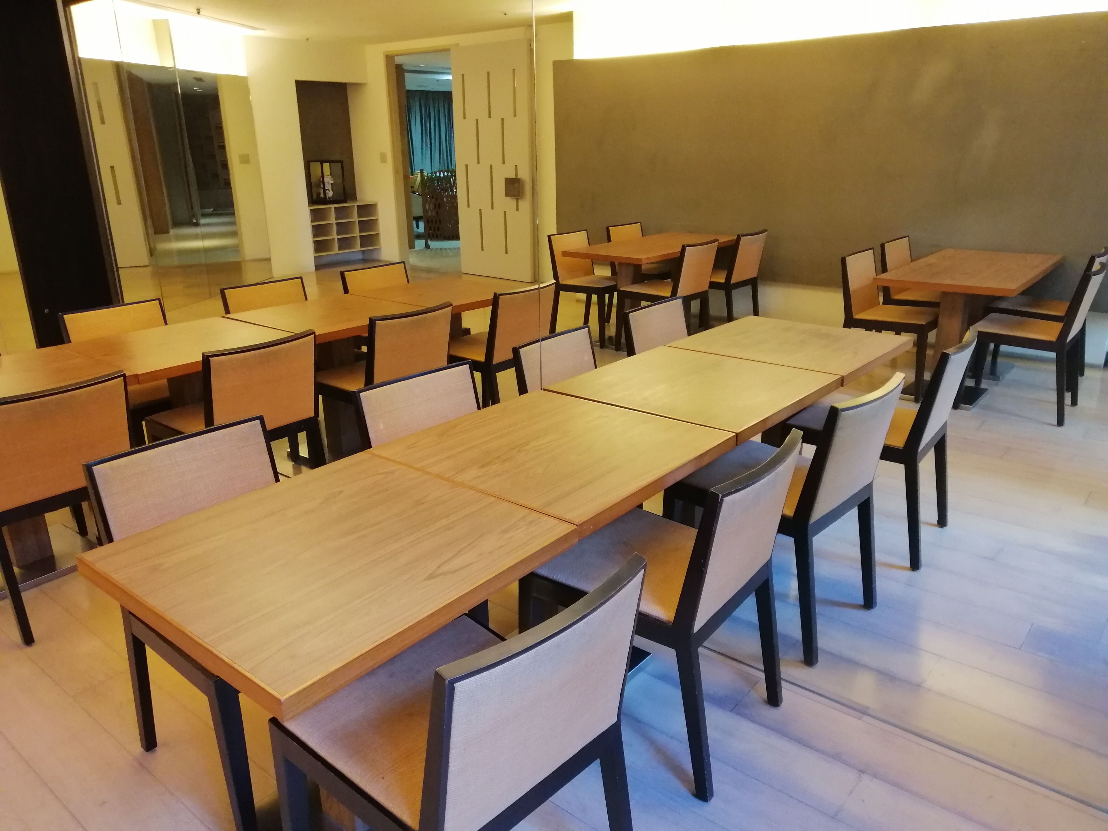 A spacious dining area with multiple wooden tables and chairs, a visible elevator, and a hallway leading to another room.