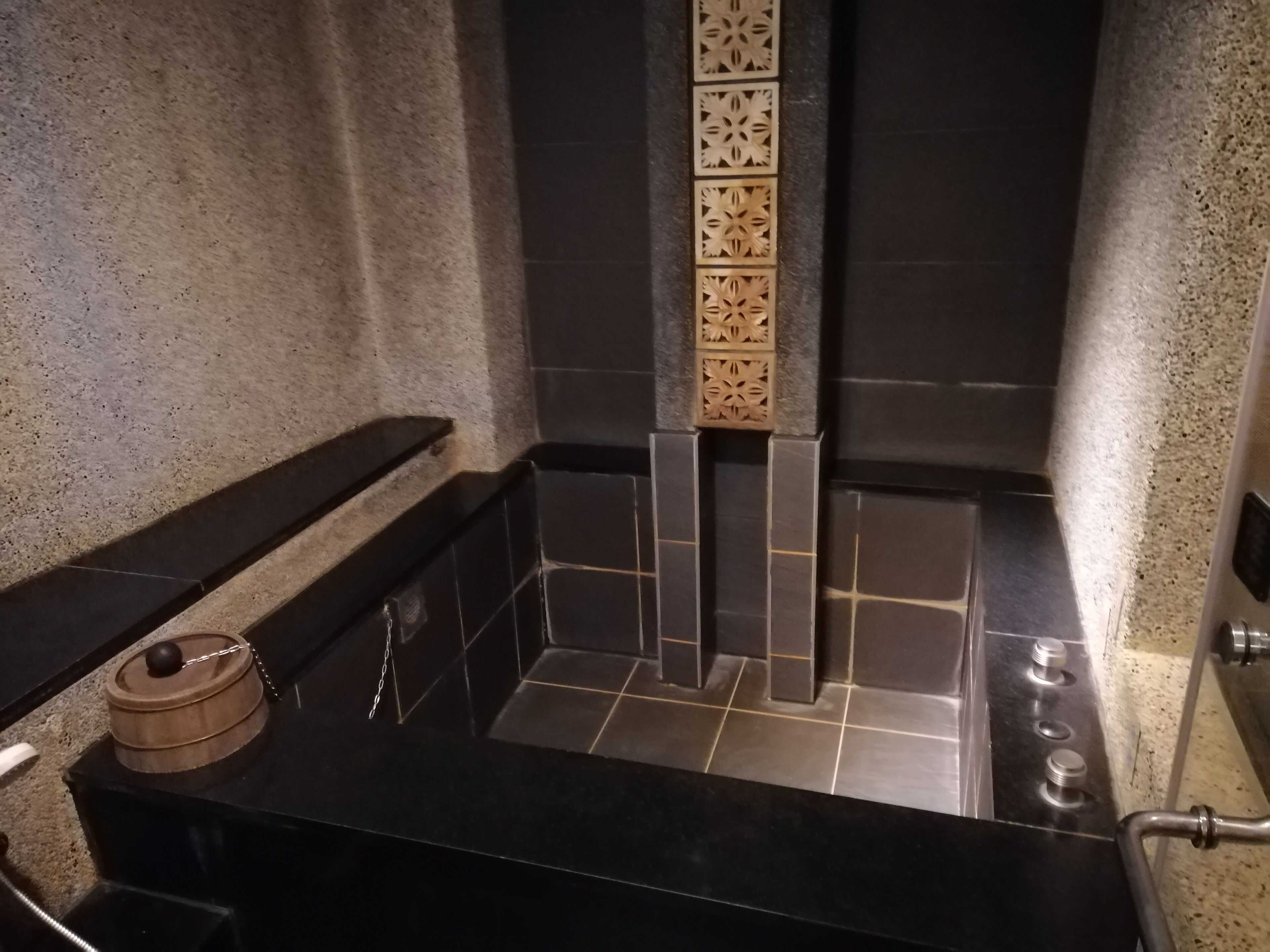 A bathroom with a black countertop, a sink, and a shower area with dark tiles and a decorative panel.