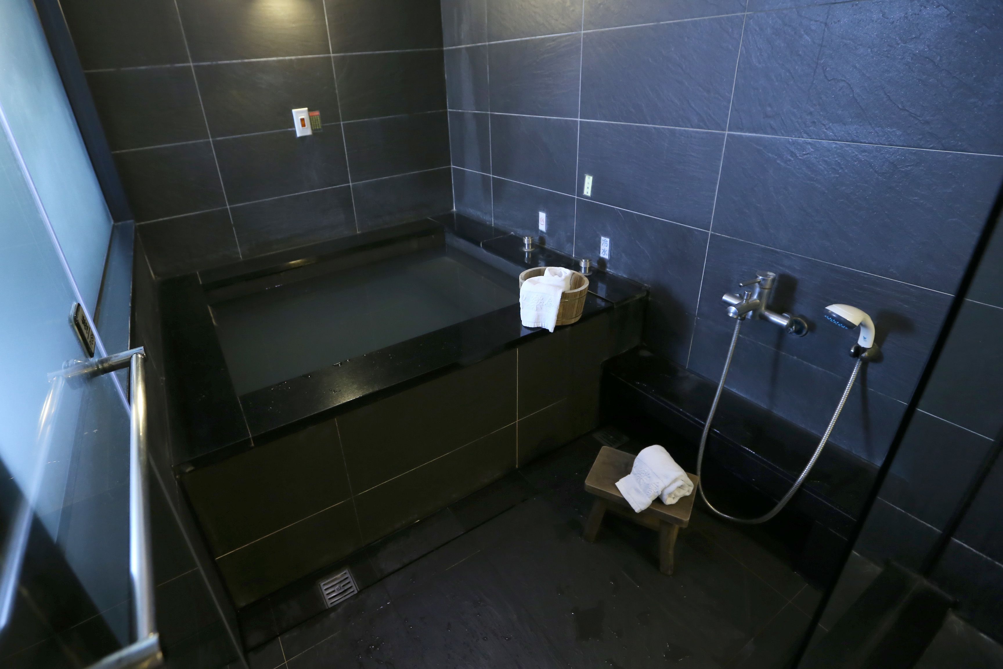 A modern bathroom with a black bathtub, a small wooden stool, and a handheld showerhead.