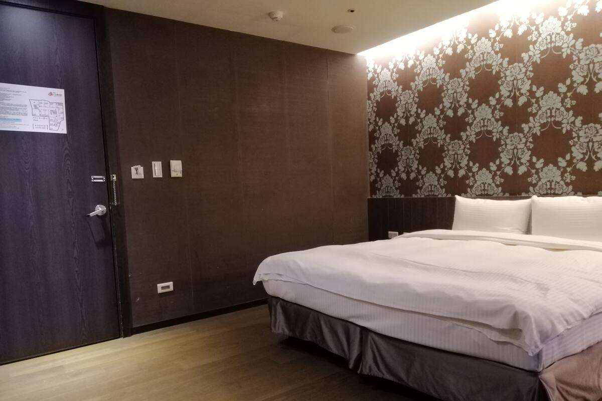 Hotellihuone, jossa on suuri sänky, vaatekaappi ja kukka-aiheinen tapetti.