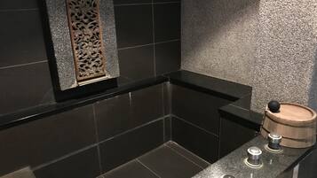 A modern bathroom with dark tiled walls, a wooden decorative panel, and a wooden barrel on the counter.