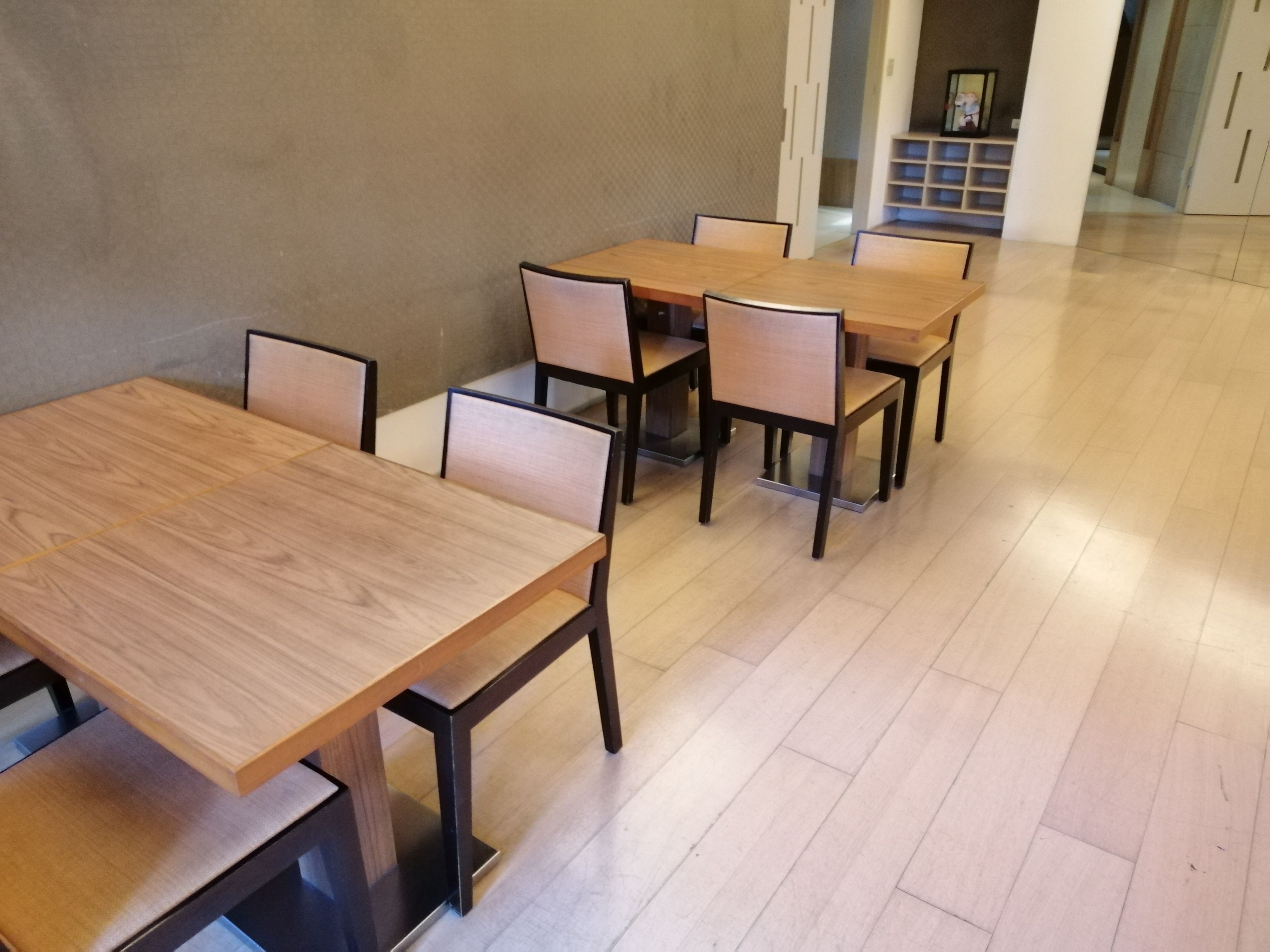 A dining area with wooden tables and chairs, a tiled floor, and a plain wall.