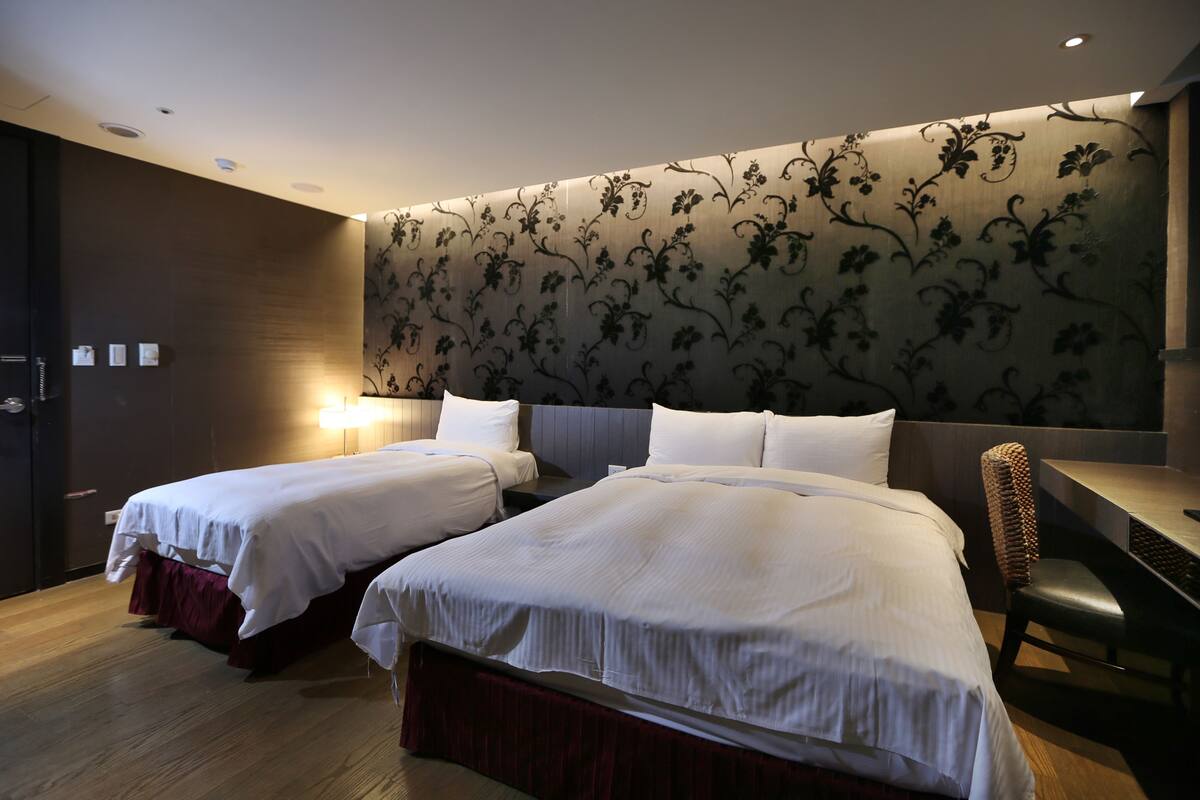 Hotellihuone, jossa on kaksi sänkyä, työpöytä ja tuoli.