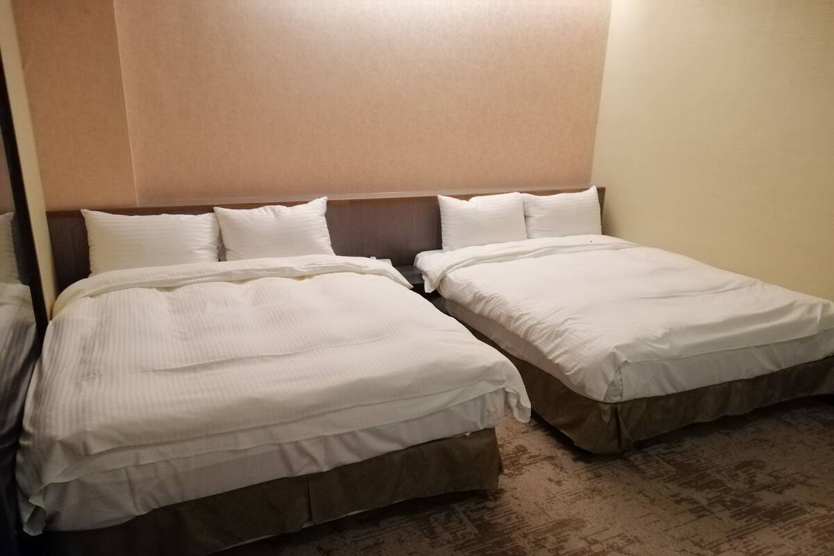 Hotellihuone, jossa on kaksi erillistä sänkyä, ja molemmissa on puinen pääty ja valkoiset vuodevaatteet.