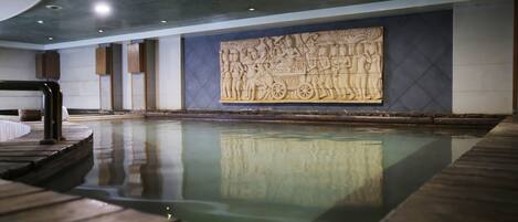 A serene indoor pool area with a wooden deck, a large wall mural, and a modern ceiling design.