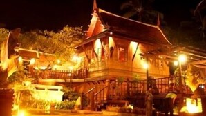 A traditional wooden building with a steeply pitched roof and a balcony, surrounded by vegetation. - Harry's Bungalows & Restaurant (Koh Samui)