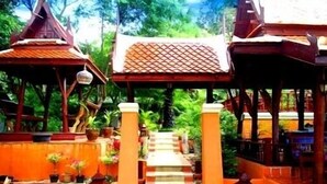A traditional wooden structure with a tiled roof, surrounded by potted plants and a stone pathway leading to it. - Harry's Bungalows & Restaurant (Koh Samui)