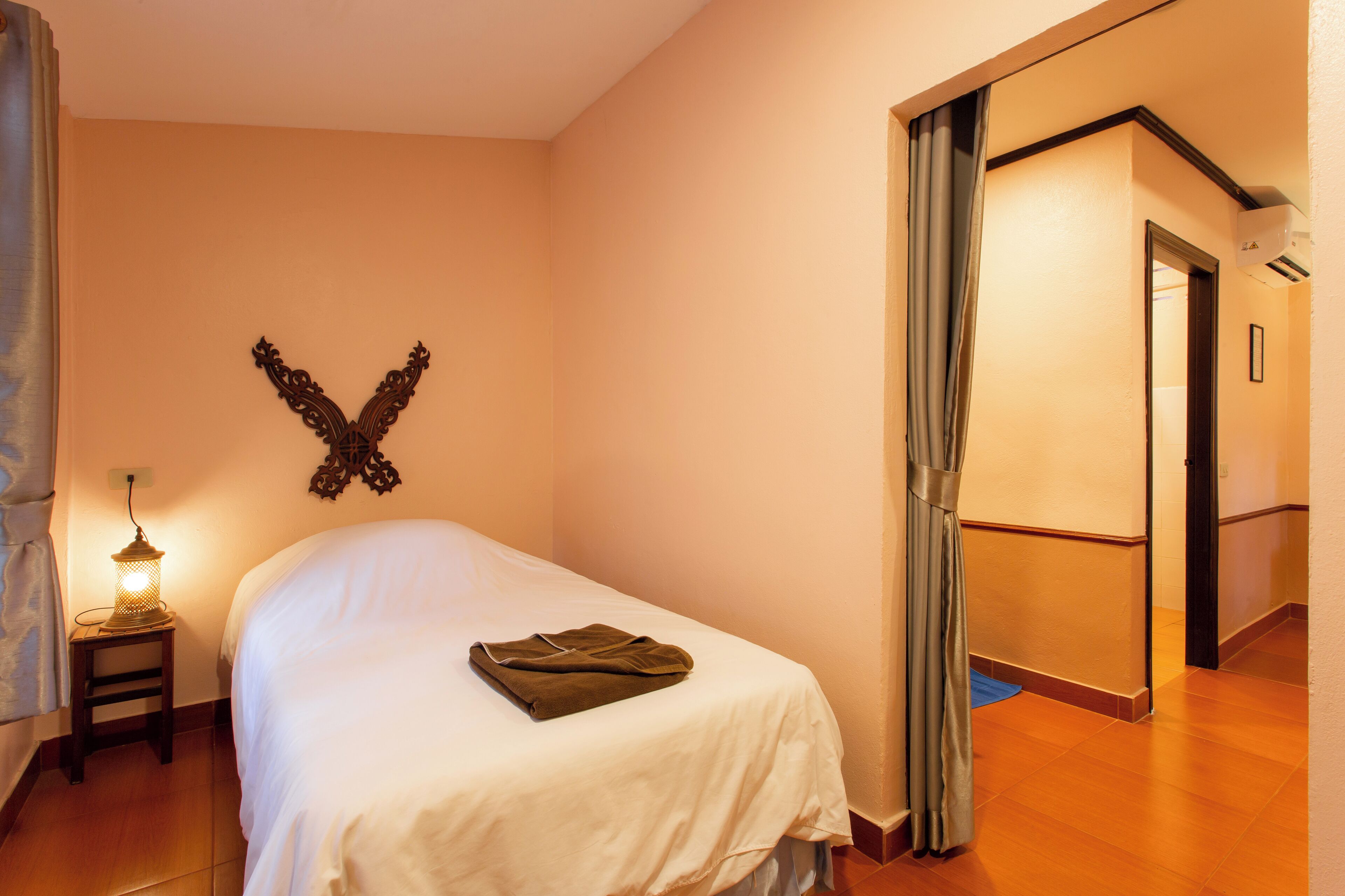 Habitación de hotel con cama, mesita de noche con lámpara, lámpara de pared y puerta que da a otra habitación.