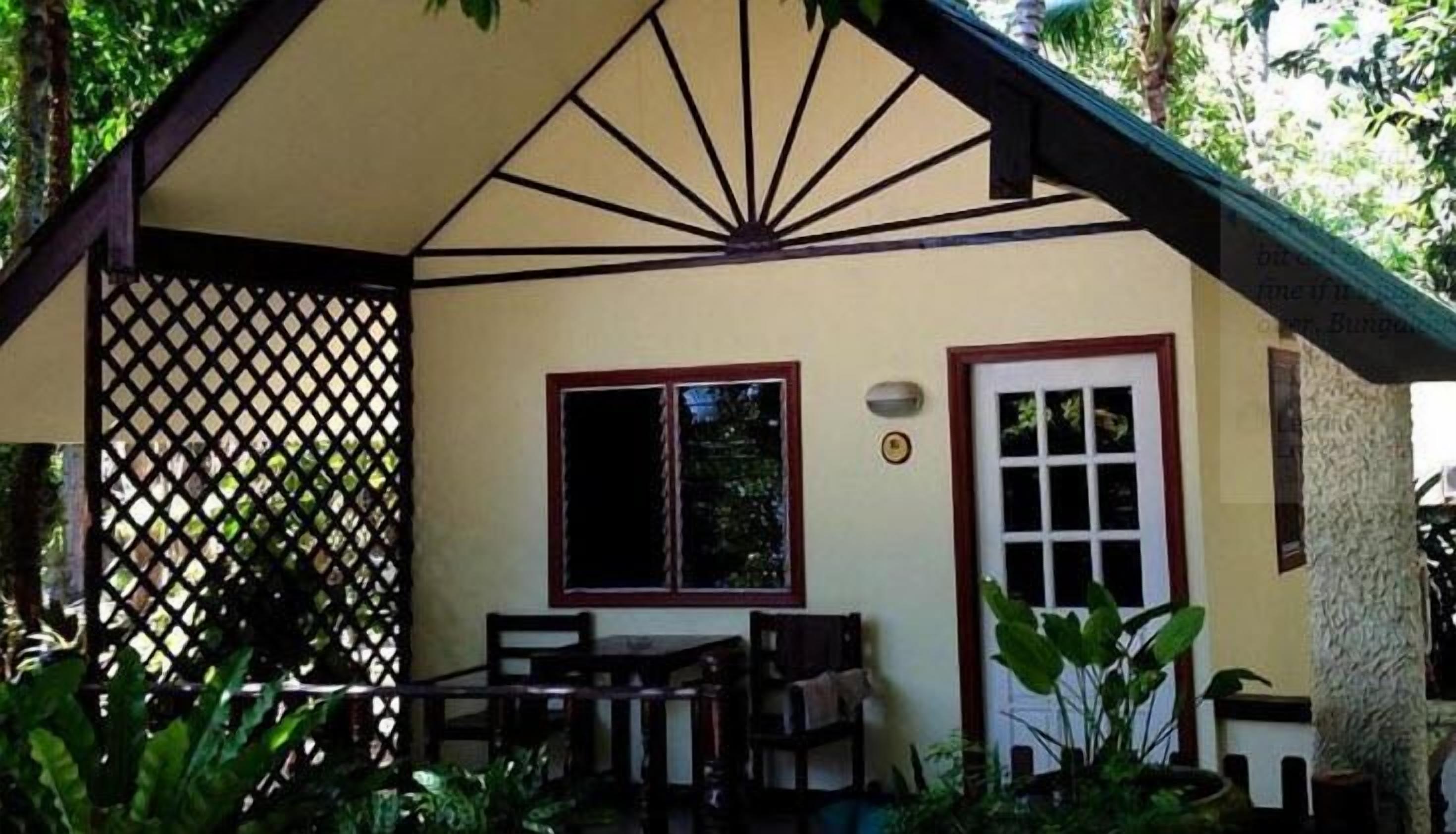 A small, single-story building with a sloped roof, a wooden table and chairs, a window, and a door.