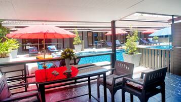 Zona de piscina con sombrillas rojas, sillas de descanso y una mesa de comedor con sillas.