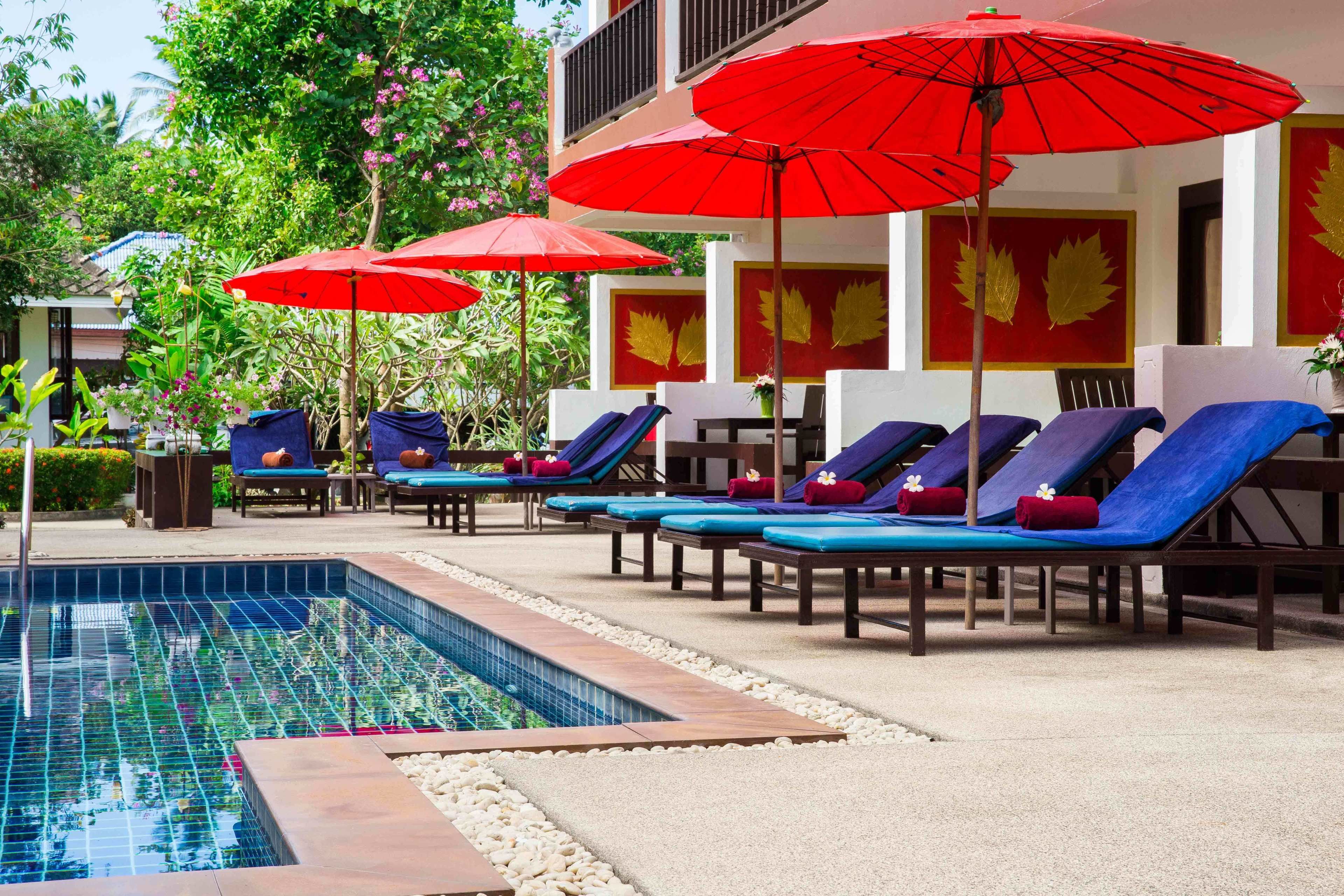 Zona junto a la piscina con sillones de descanso y sombrillas rojas.