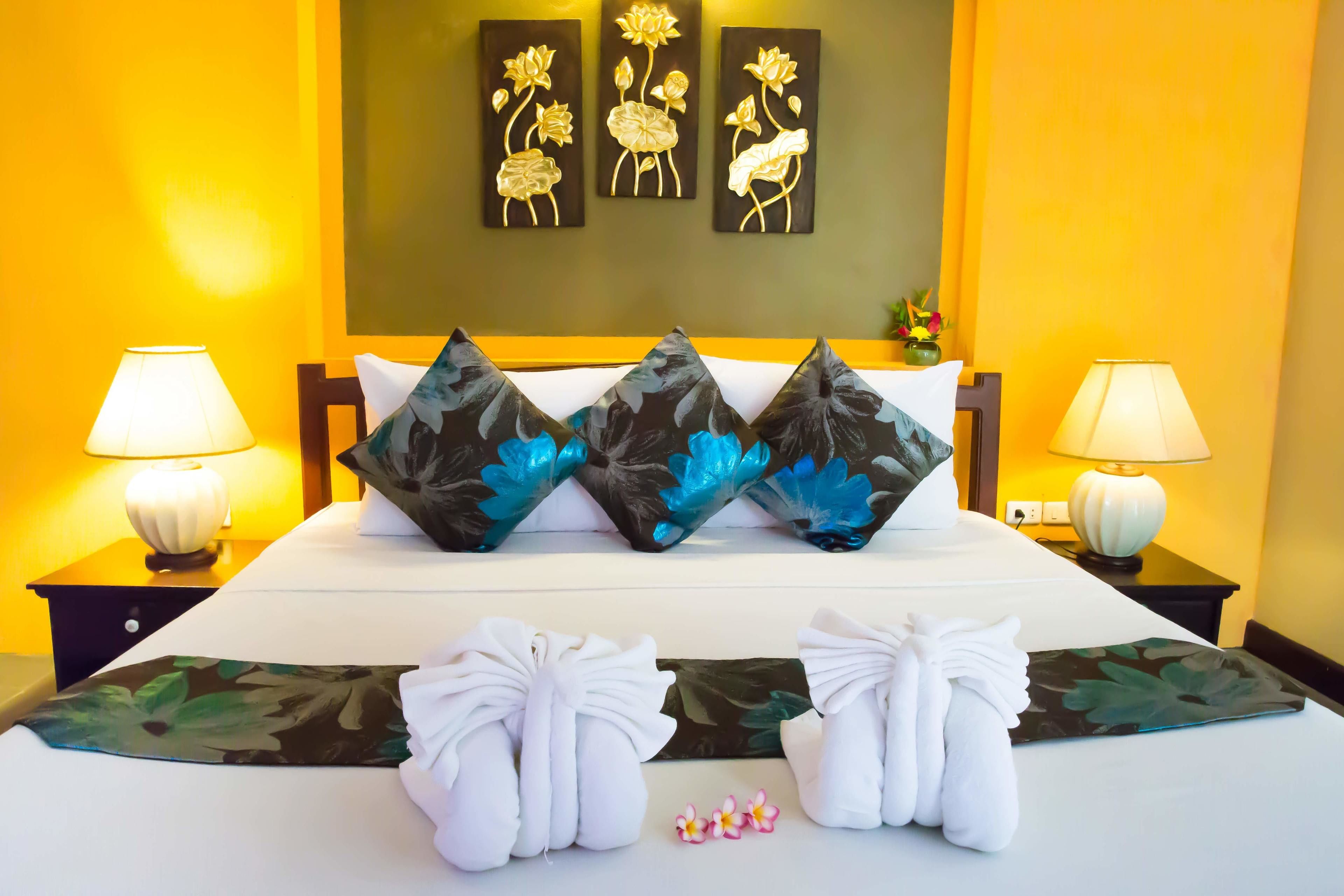 A neatly made bed with floral pillows, a pair of towels, and a wall with three flower paintings.