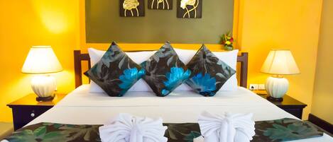 A neatly made bed with floral pillows, a pair of towels, and a wall with three flower paintings.