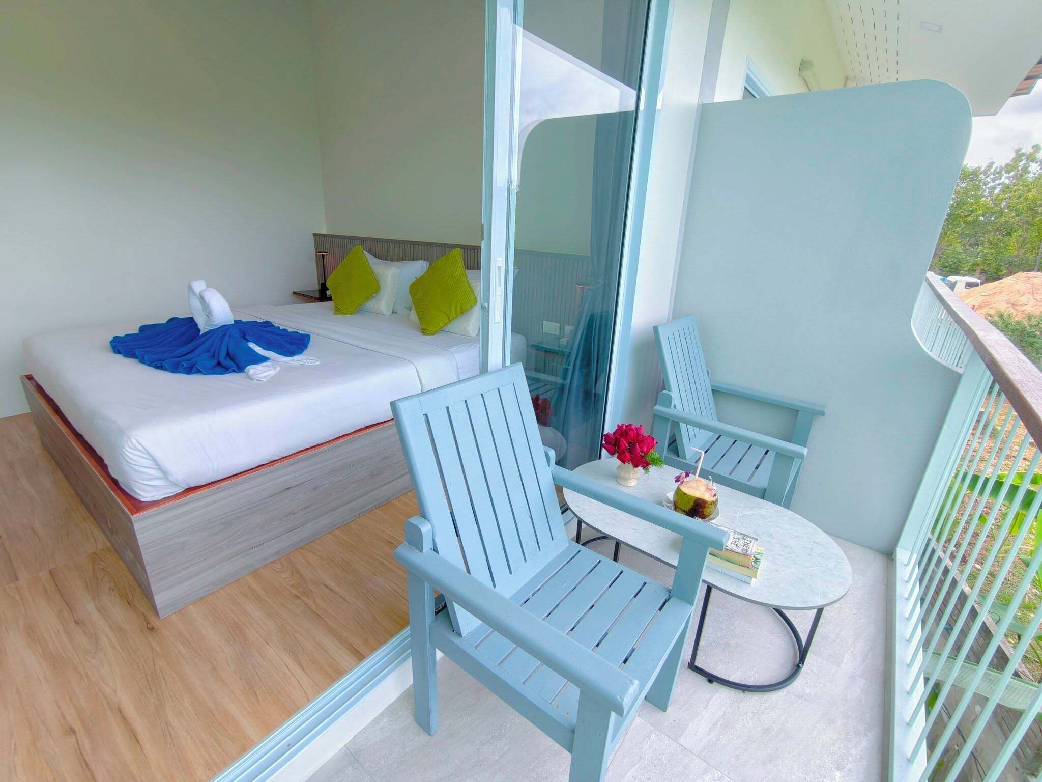 Un balcone con un letto, due sedie blu, un tavolino e vista sul verde.