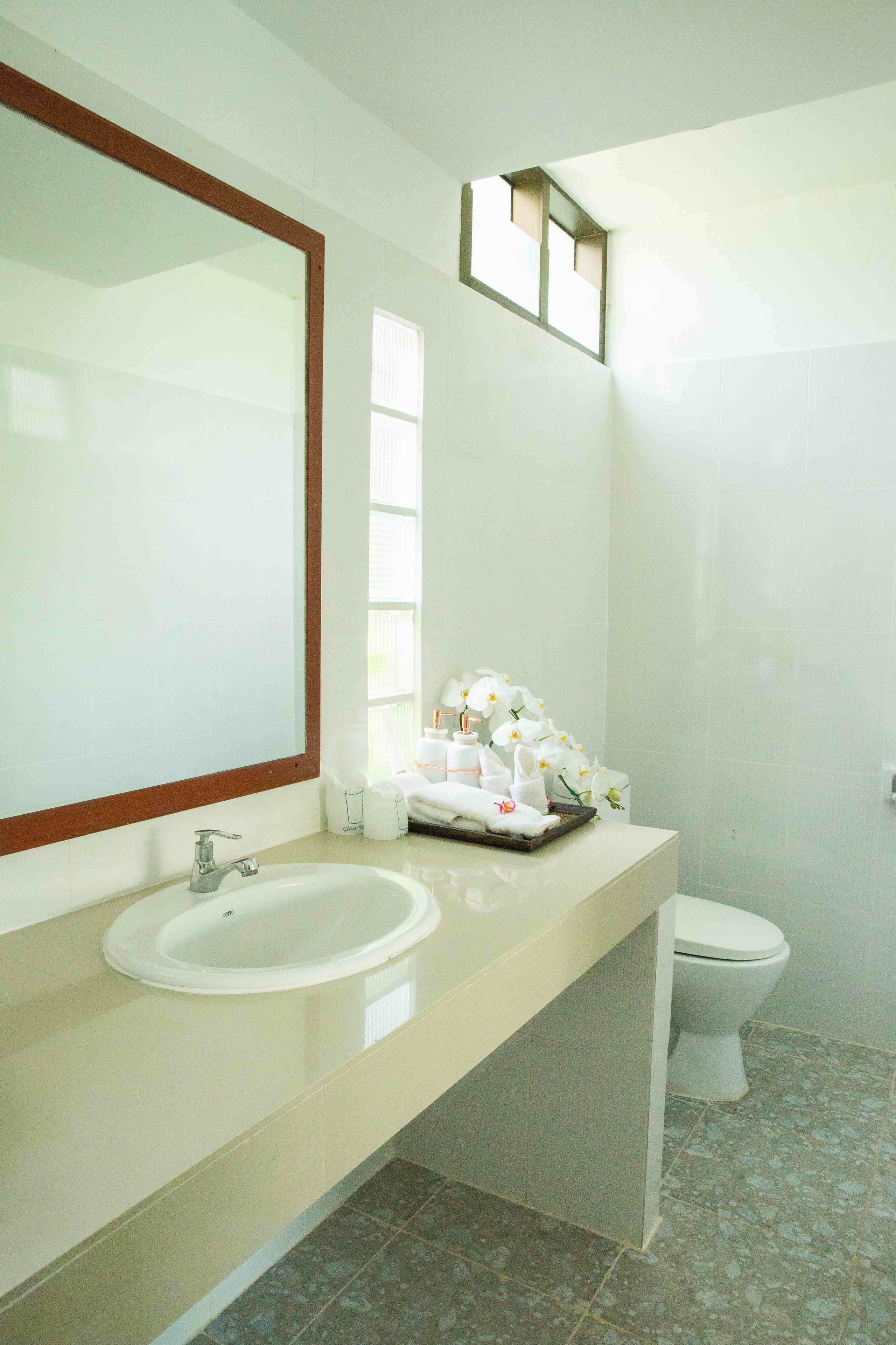 Ein Badezimmer mit großem Spiegel, Waschbecken, Toilette und kleinem Fenster.