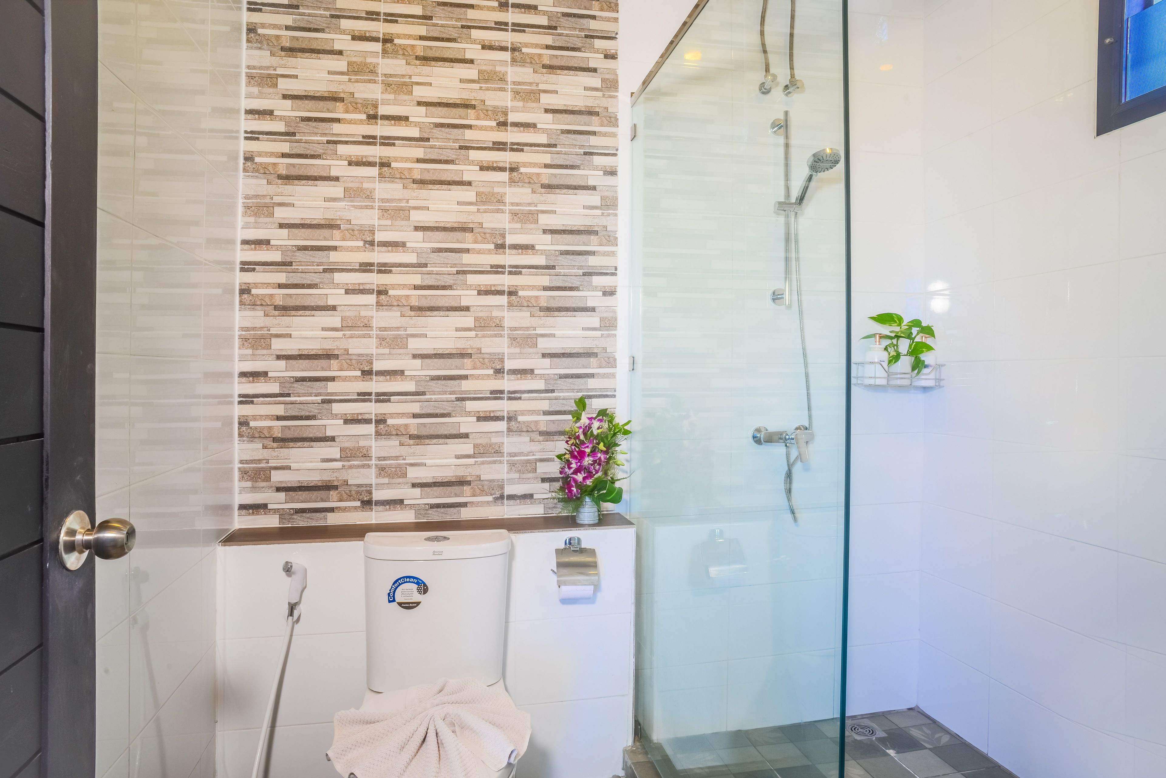 A modern bathroom with a glass shower enclosure, a toilet with a paper towel dispenser, and a decorative tile backsplash.
