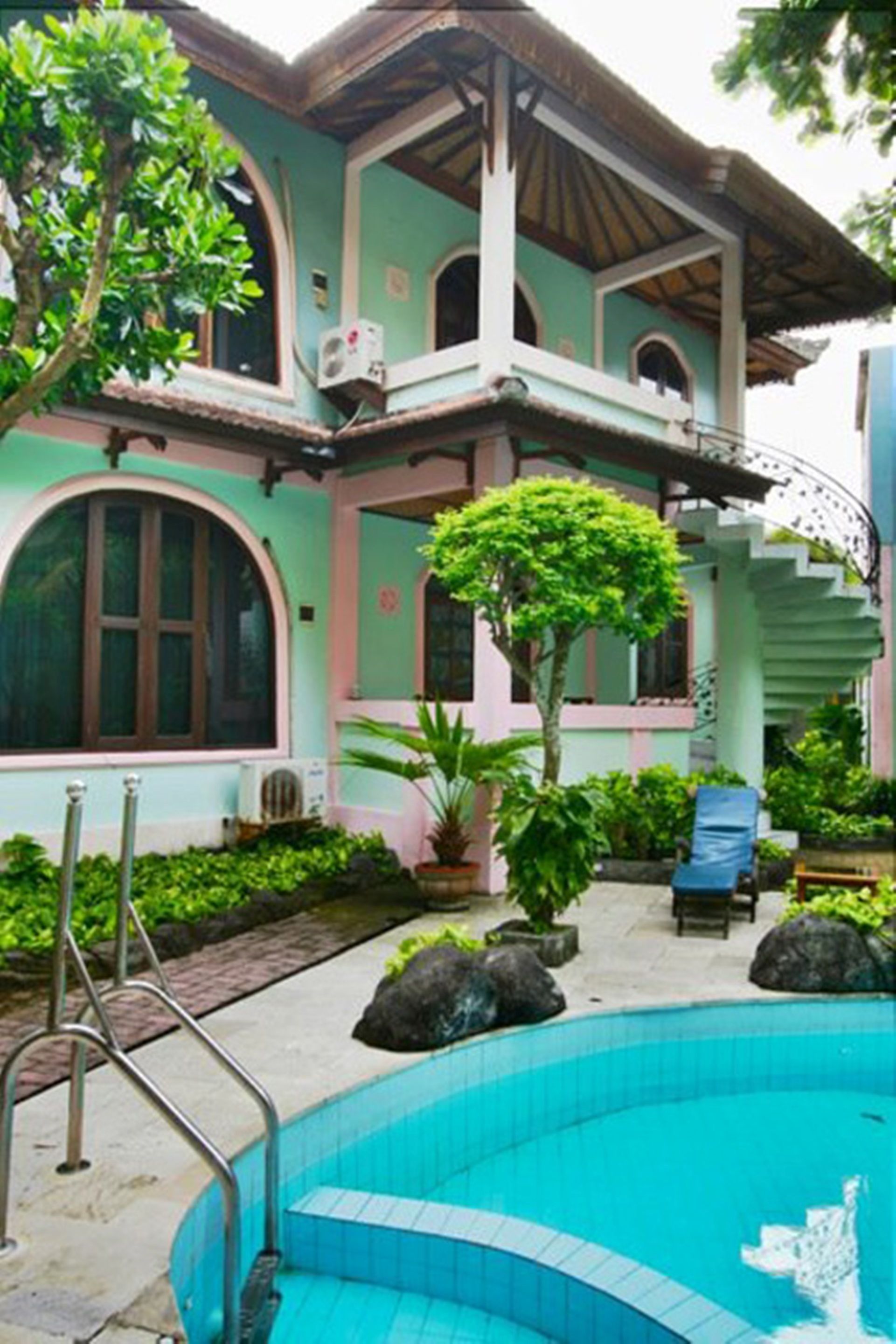 A two-story house with a swimming pool, surrounded by greenery and potted plants.