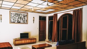 A living room with a television, wooden furniture, a ceiling fan, and a large painting on the wall.