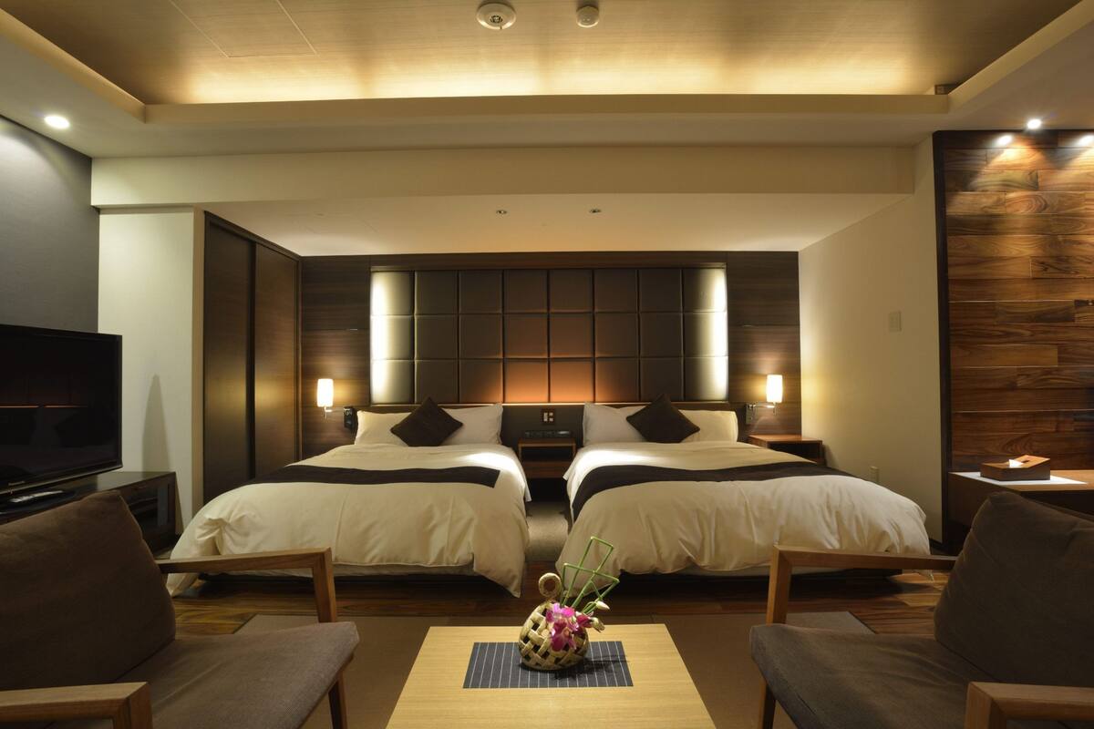 A hotel room with two beds, a TV, and a seating area with a table.