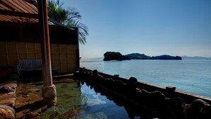 Una piscina cristalina con rocas, una terraza de madera y vistas al mar y a islas lejanas.