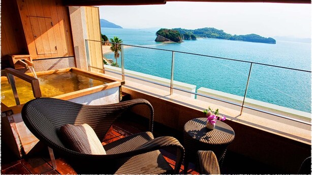 Un balcón con mobiliario de mimbre, una mesa pequeña con un florero, y vistas al mar y a las islas.