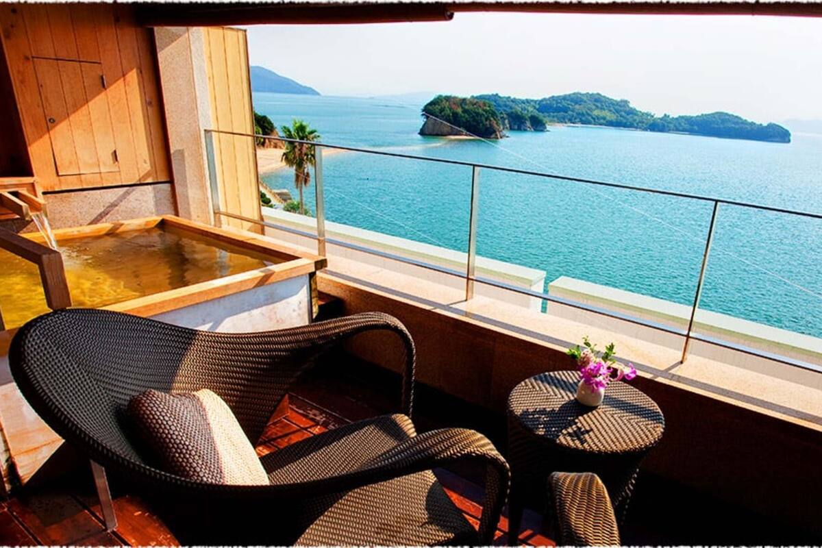 A balcony with wicker furniture, a small table with a vase, and a view of the sea and islands.
