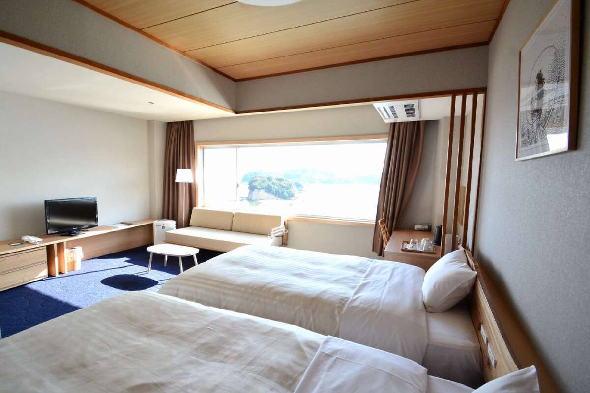 A hotel room with two beds, a desk with a television, a small table, and a window with curtains.