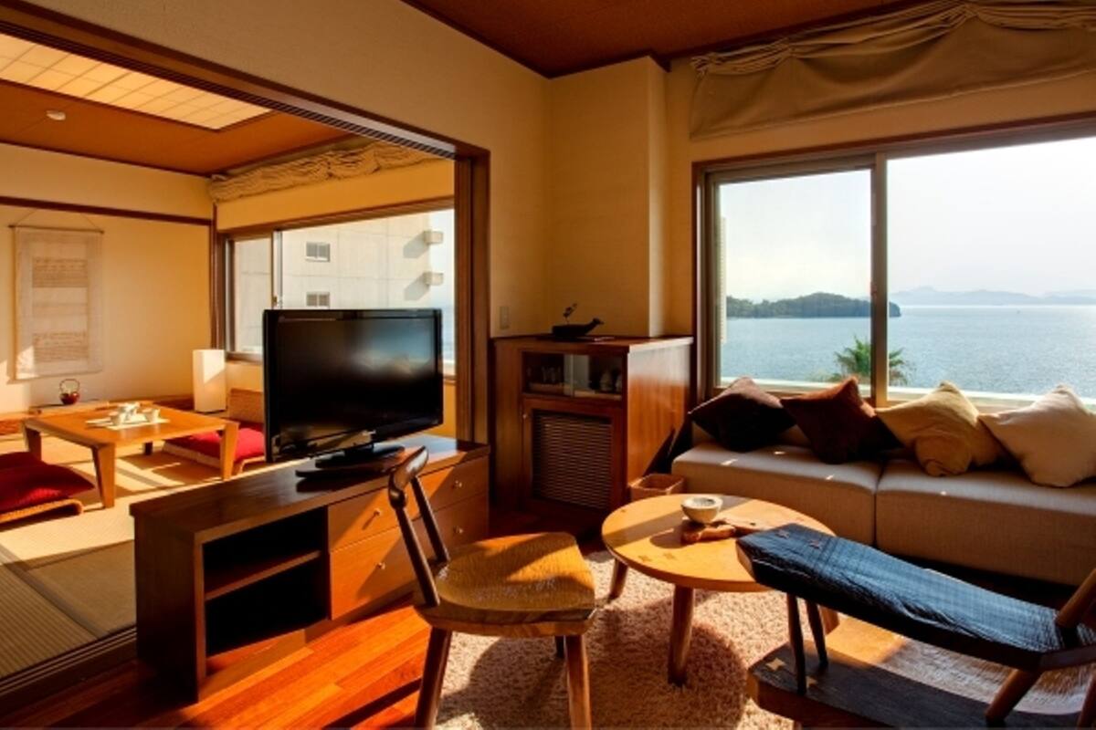 A room with a TV, sofa, and a view of the sea.