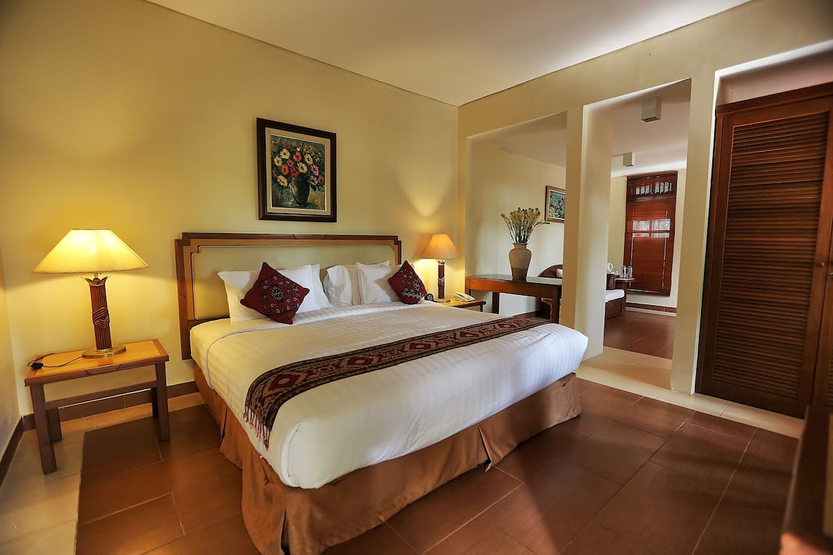 Habitación de hotel con una cama grande, dos mesitas de noche con lámparas, un cuadro en la pared y una puerta de madera.