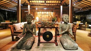 Una construcción de madera tradicional con un ventilador de techo, una mesa con un adorno y dos estatuas.
