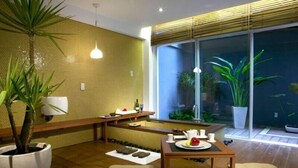 Un interior moderno con un banco de madera, una mesa con tetera y tazas, y un amplio ventanal con vistas a un jardín.