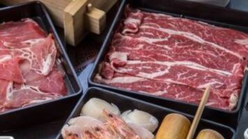 A hot pot setup with various meats, seafood, vegetables, and condiments.