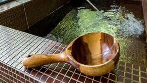 Un área de aguas termales con un cucharón de madera, paredes de azulejos y una ventana con vistas a la vegetación.