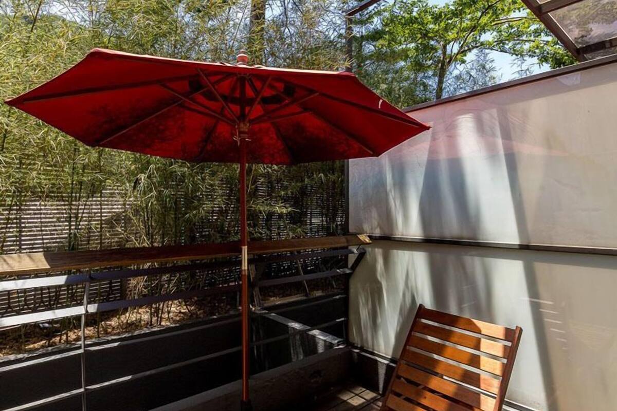 A wooden deck with a red umbrella, a wooden chair, and a metal railing.
