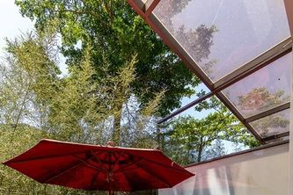 A wooden deck with a red umbrella, a wooden bench, and a glass enclosure.