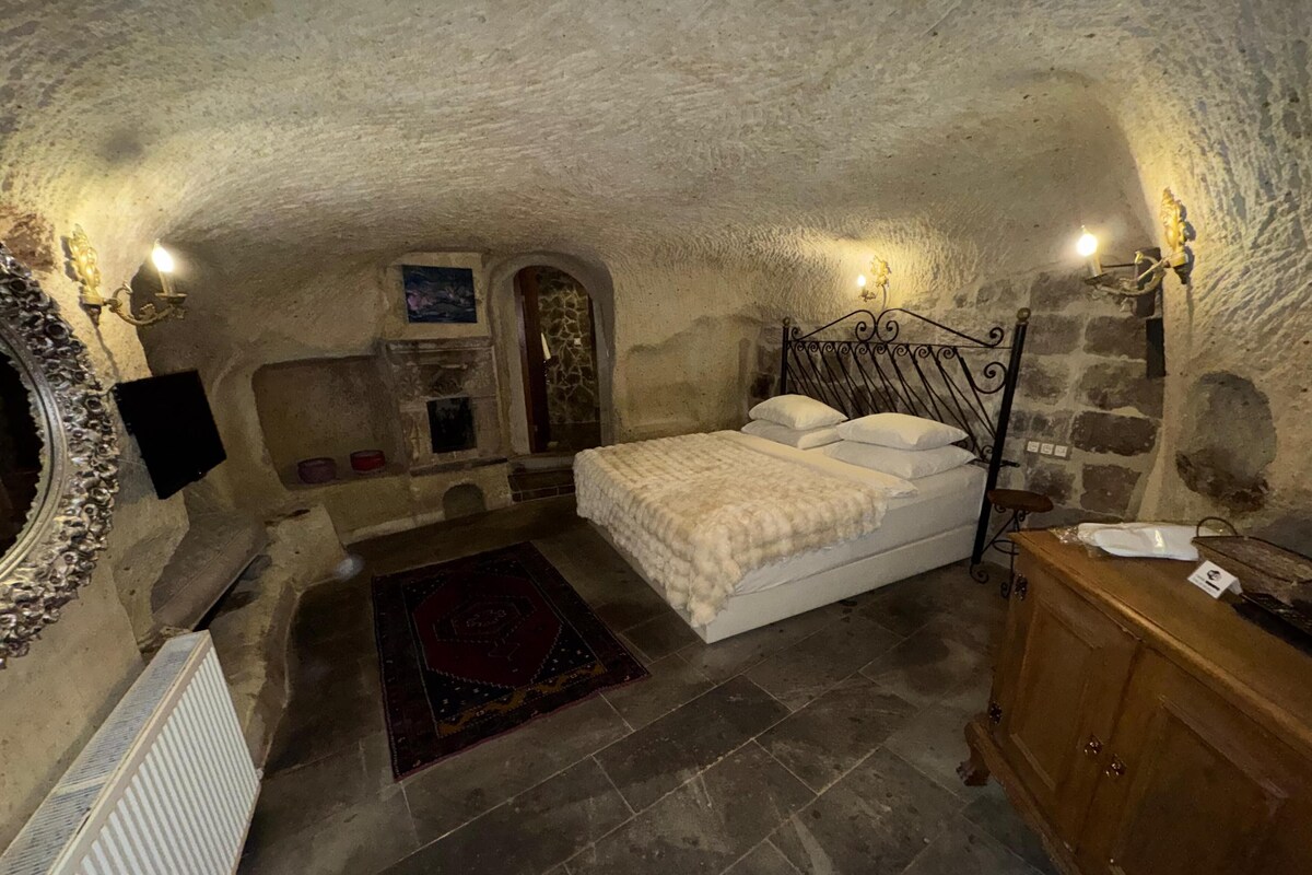 A cozy, stone-walled bedroom with a bed, a wooden dresser, and a stone fireplace.