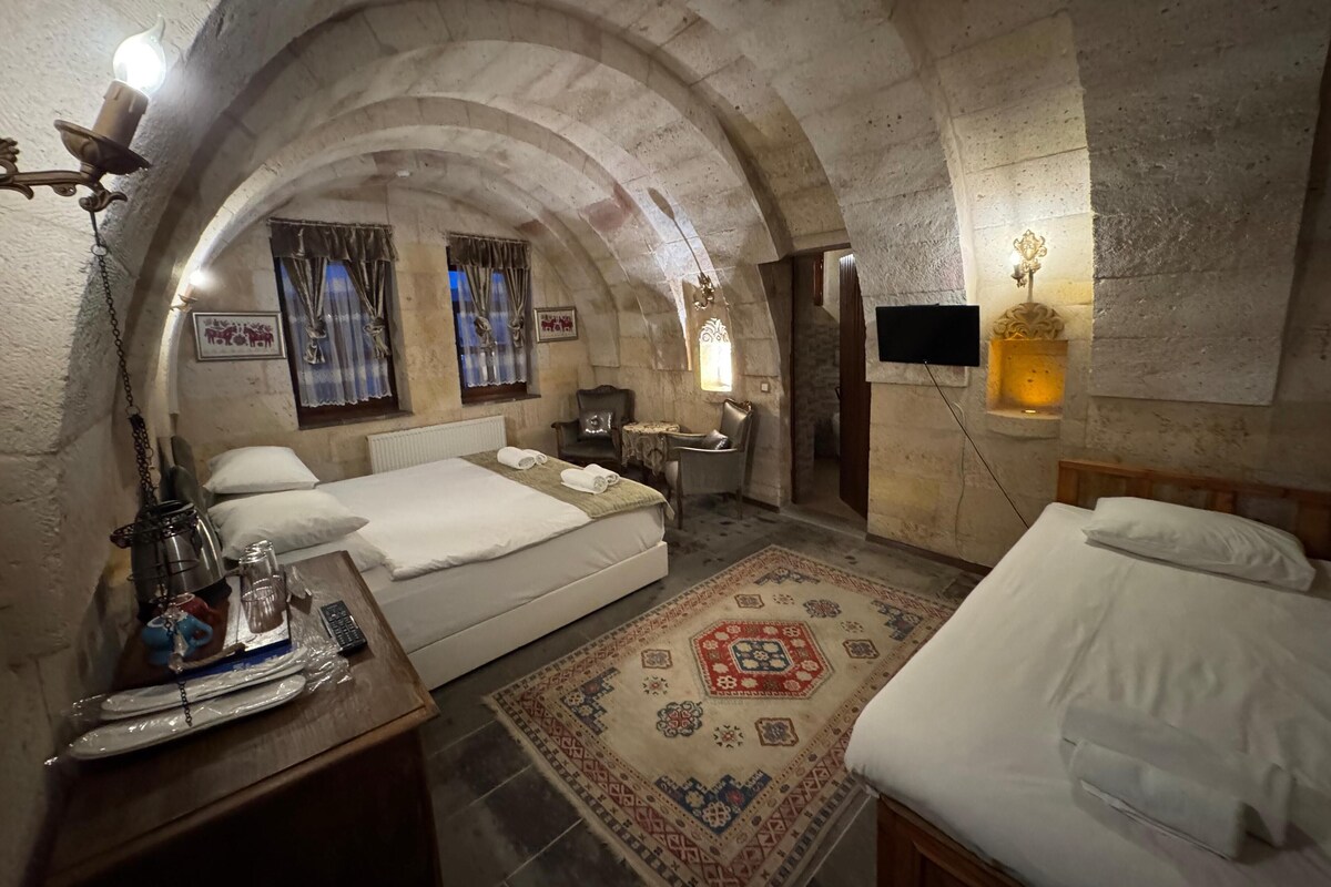 A room with two beds, a small table, a chair, a TV, and a decorative rug.