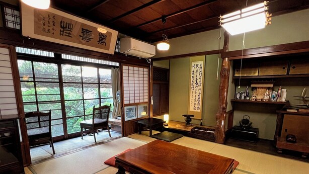Una habitación japonesa tradicional con suelo de tatami, una mesa de madera, una silla y una puerta corrediza que da a un balcón.