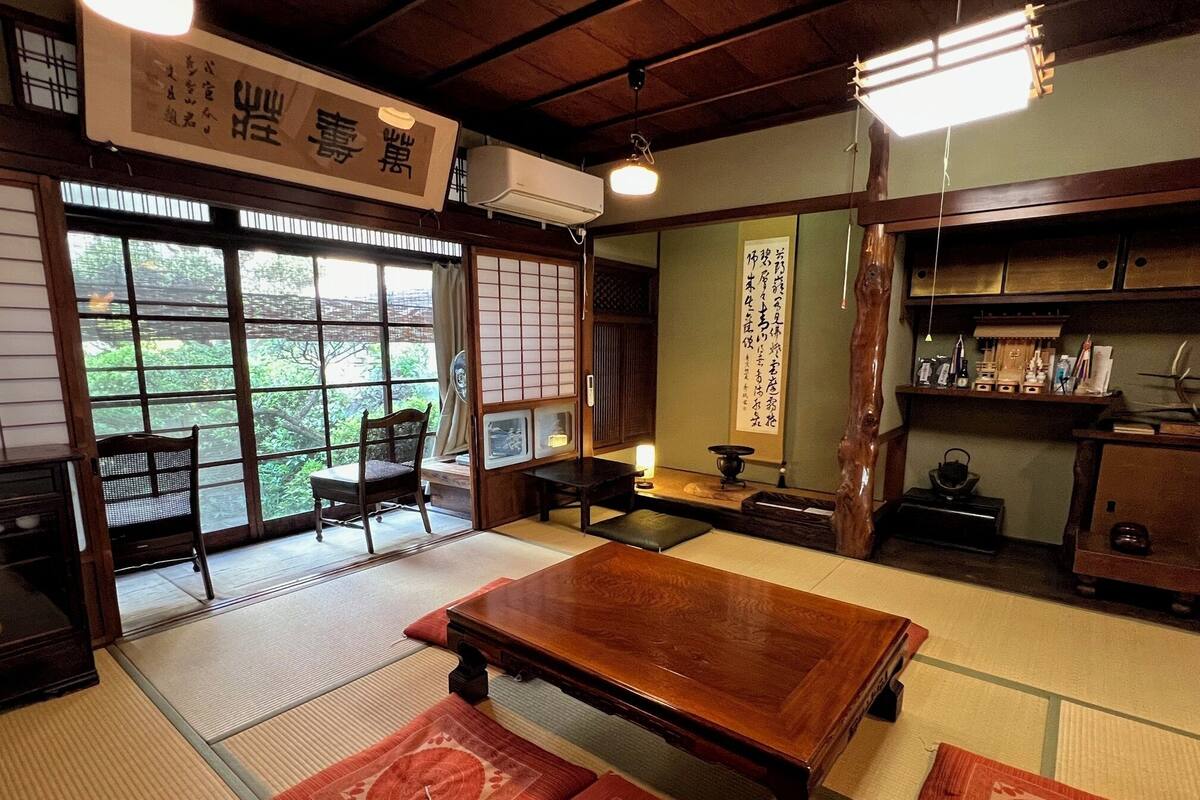 A traditional Japanese room with tatami flooring, a wooden table, a chair, and a sliding door leading to a balcony.